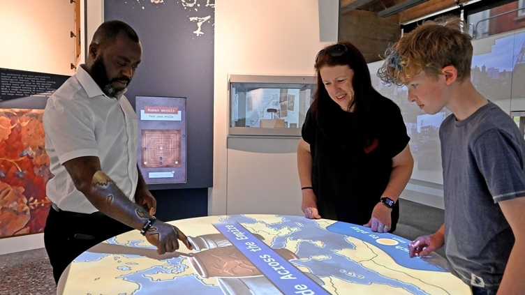 Three people looking at an interactive exhibit in a museum of Roman Britain