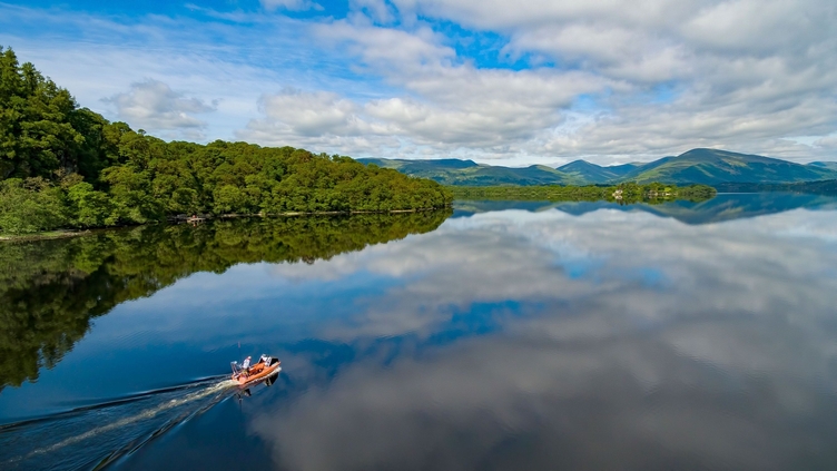 A man powers a motor boat on the waters of Loch Lomond.