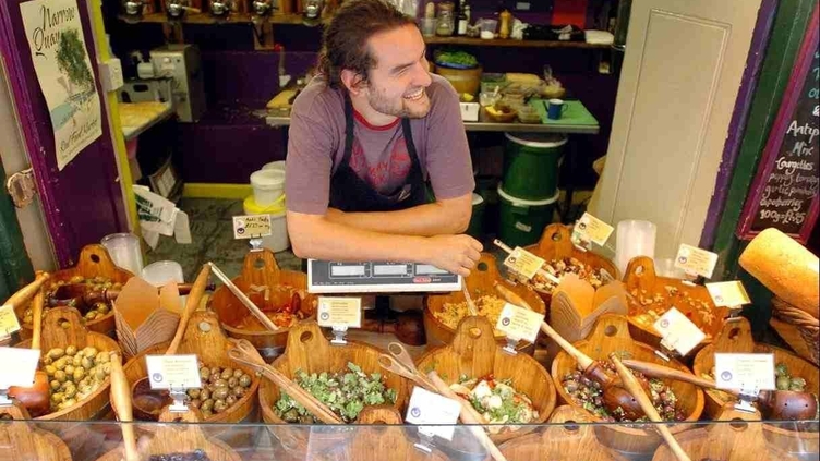 A market trader selling many varieties of olives from a stall