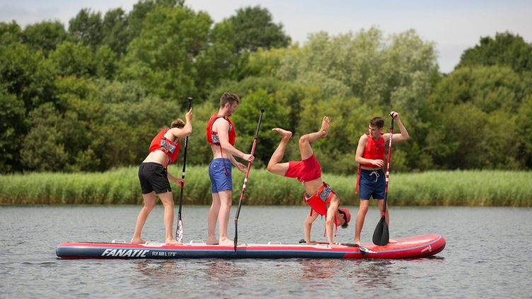 Four men in red life vests standing on a paddleboard