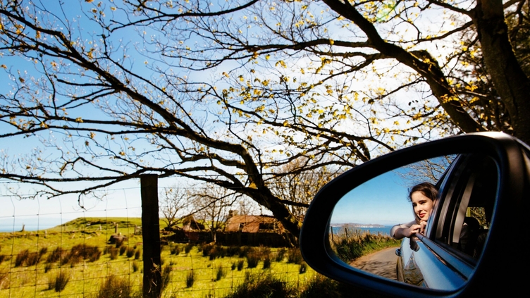 Woman seen in the car wing mirror as she looks out of the car window 
