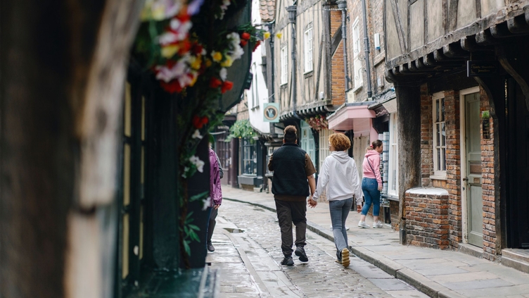 A man and a woman walk down a cobbled street holding hands
