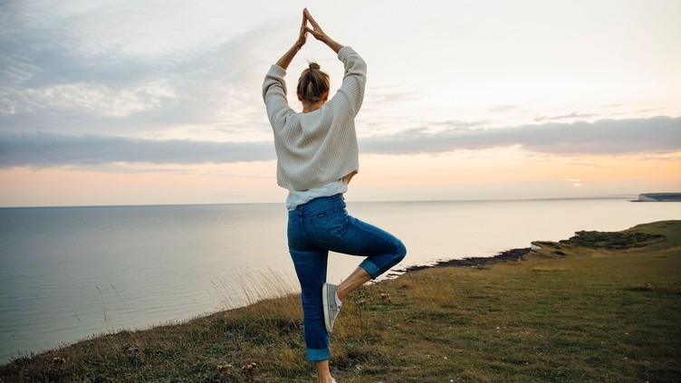Vista trasera de una mujer en postura de yoga en lo alto de un acantilado