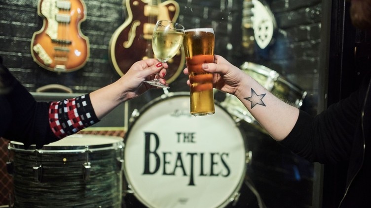 Nahaufnahme von zwei Personen, die mit Weißwein und Bier anstoßen