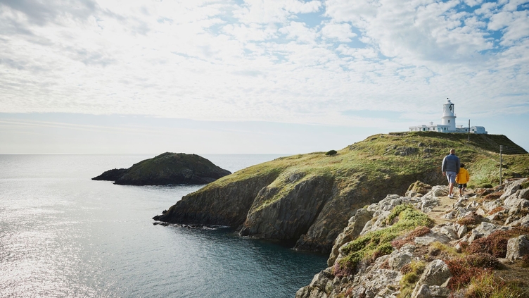 People walking on coastal path towards a lighthouse