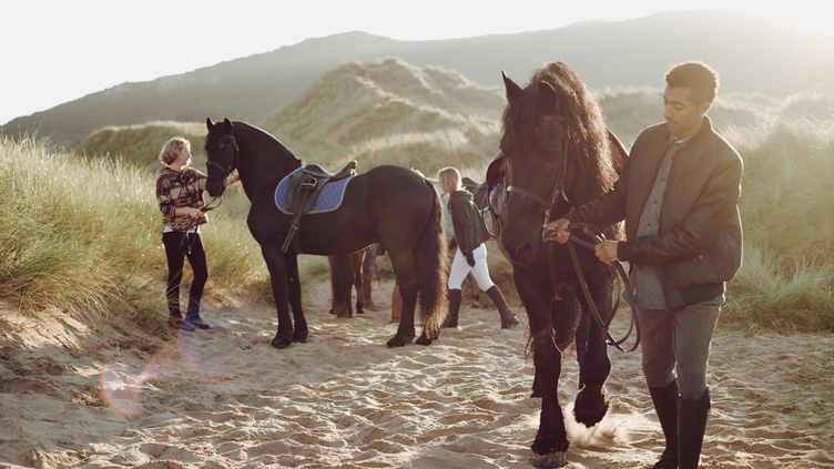People leading horses along beach by their harness
