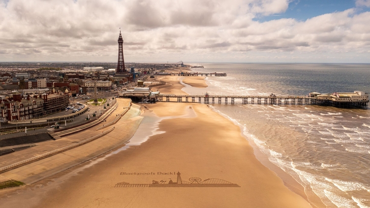 Landscape shot of a sandy beach with a pier and tower.