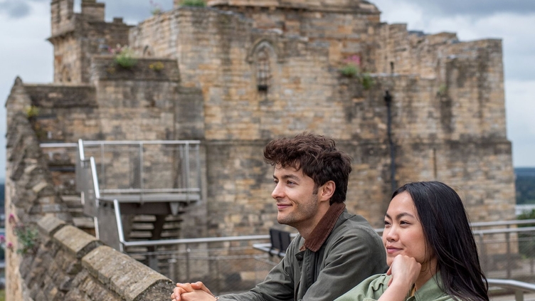 A man and a woman look out to a view from a castle