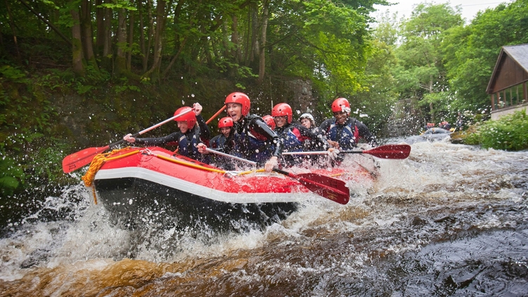 People wearing wetsuits and helmets paddling down a rapid