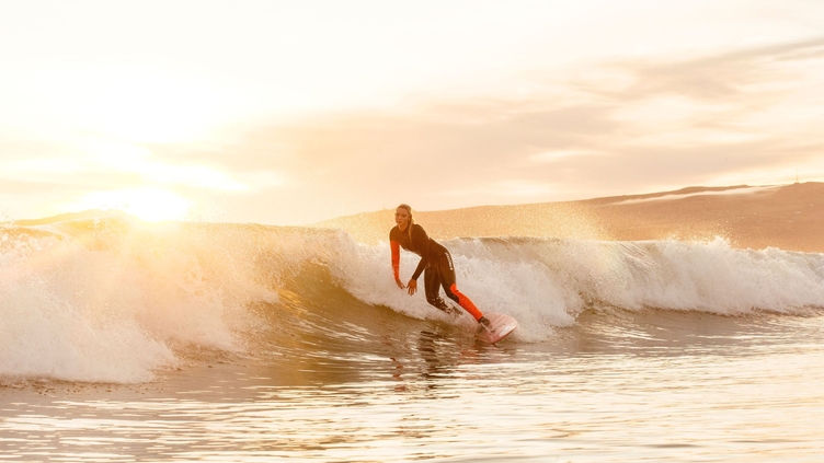 Woman, in black and red wetsuit, surfing a small wave