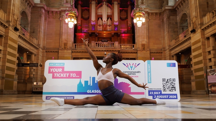 A female gymnast stretching in front of an oversized Commonwealth Games ticket, inside an art gallery 