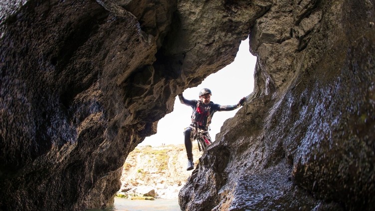 People coasteering at Stair Hole in the limestone cliffs along the shores of the Jurassic coastline near Lulworth Cove in Dorset. People climbing up the rocks.
