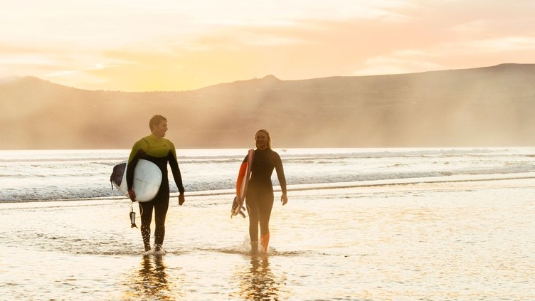 Young man and woman, carrying surfboards on the beach