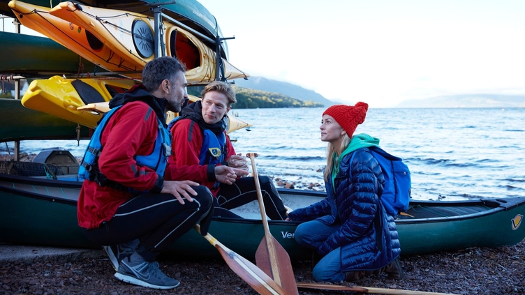 A group of people on the shore, with a stack of kayaks