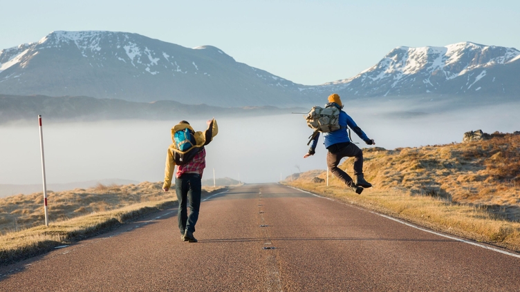 Rear view of two men jumping with joy on a country road 