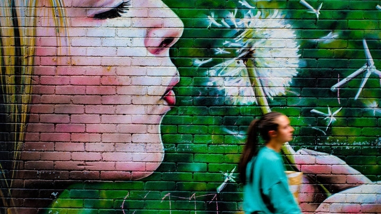 A woman walking beside a street art piece on the Glasgow Mural Trail