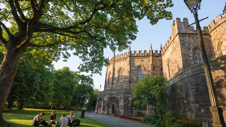 External view of Lancaster castle with visitors sitting around the lawn in the foreground