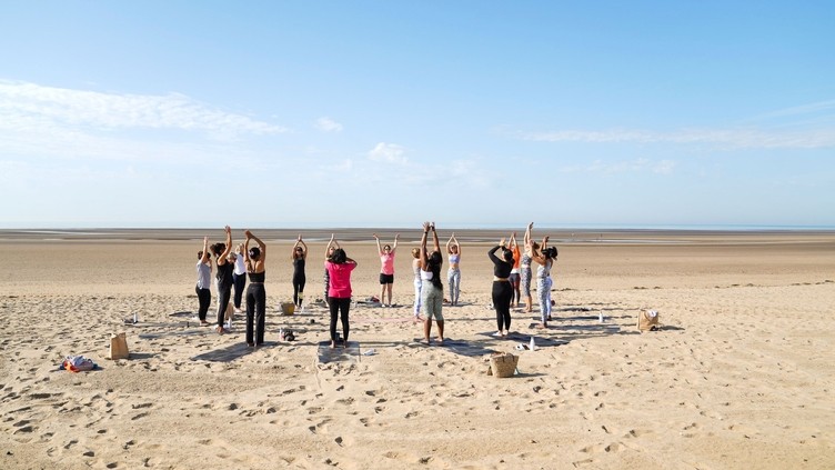 A group of adults in a circle on the beach practising yoga