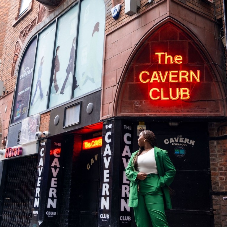 A woman poses on sidewalk outside of The Cavern Club neon sign.