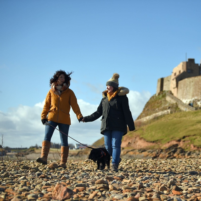 Visitors walking with their dog at Lindisfarne Castle, Northumberland