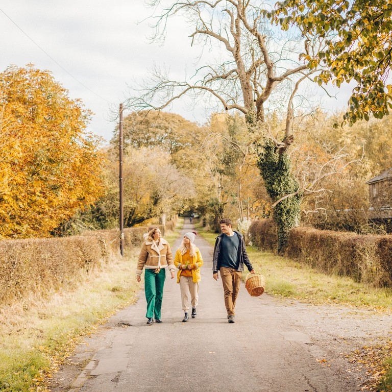 Zwei Frauen und ein Mann gehen auf einem Feldweg im Herbst spazieren