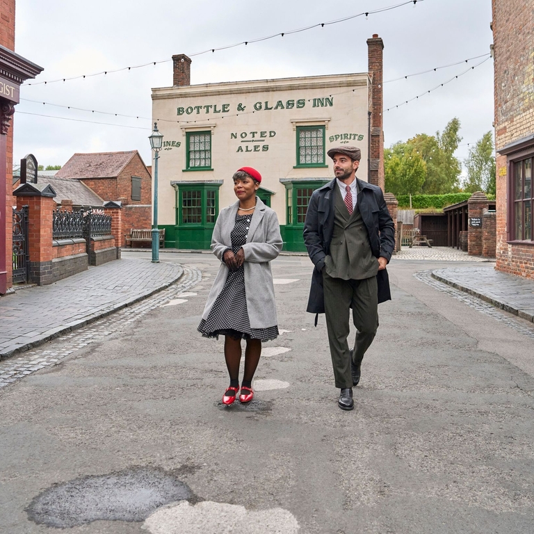 A man and woman walking through a street at a living museum