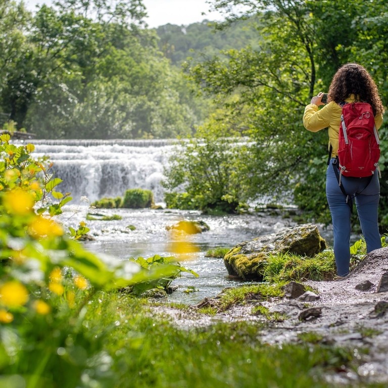 A woman stand by a waterfall and takes a picture