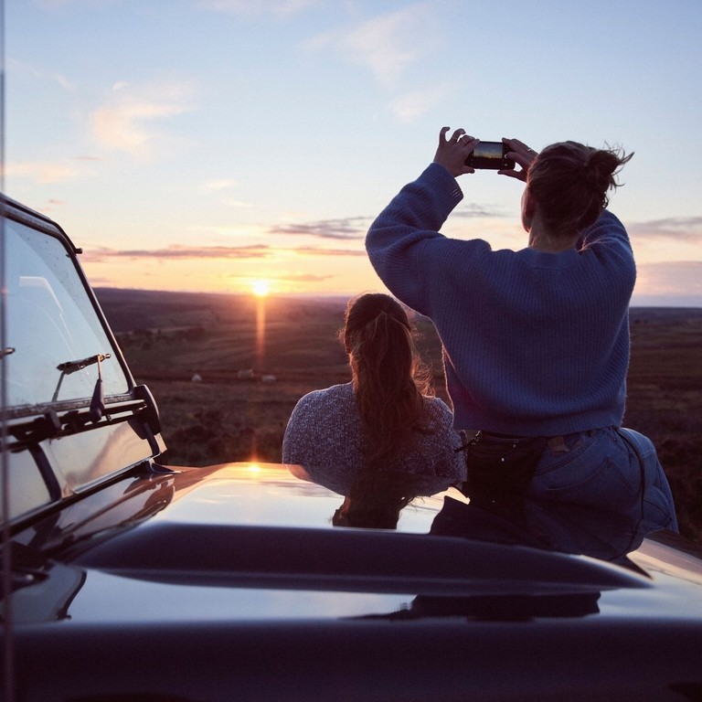 Femmes assises sur le capot d'une voiture 4x4 garée sur la route au coucher du soleil
