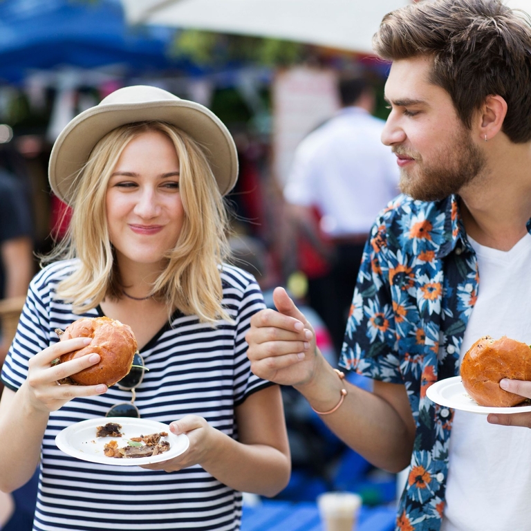 Couple eating burgers at food market.