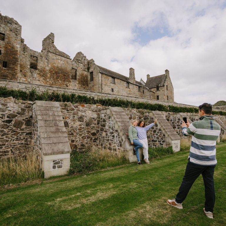 A man taking a picture of two women in the grounds of old castle ruins.