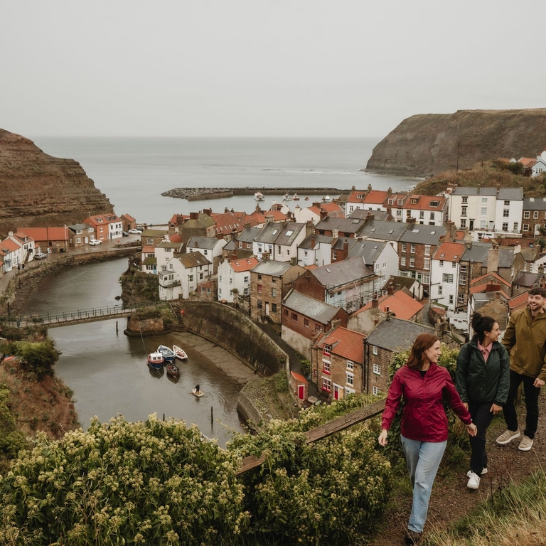 Four people looking over a coastal town nestled among the cliffs by a river mouth with the sea on the horizon