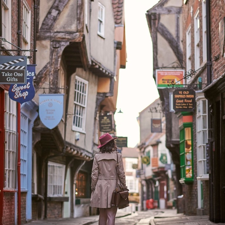 Donna con cappello rosa che cammina in una strada stretta