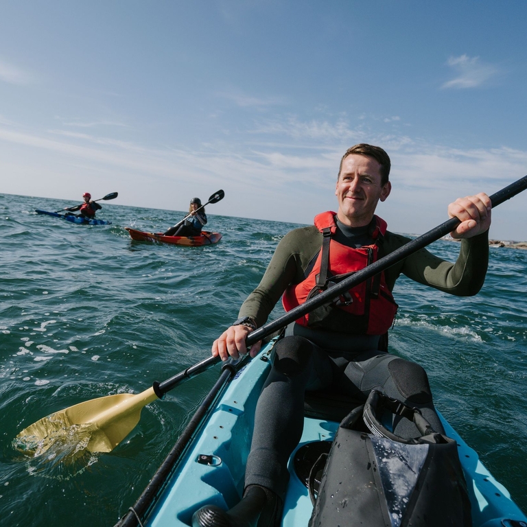 A man kayaking with two other people kayaking in the background.