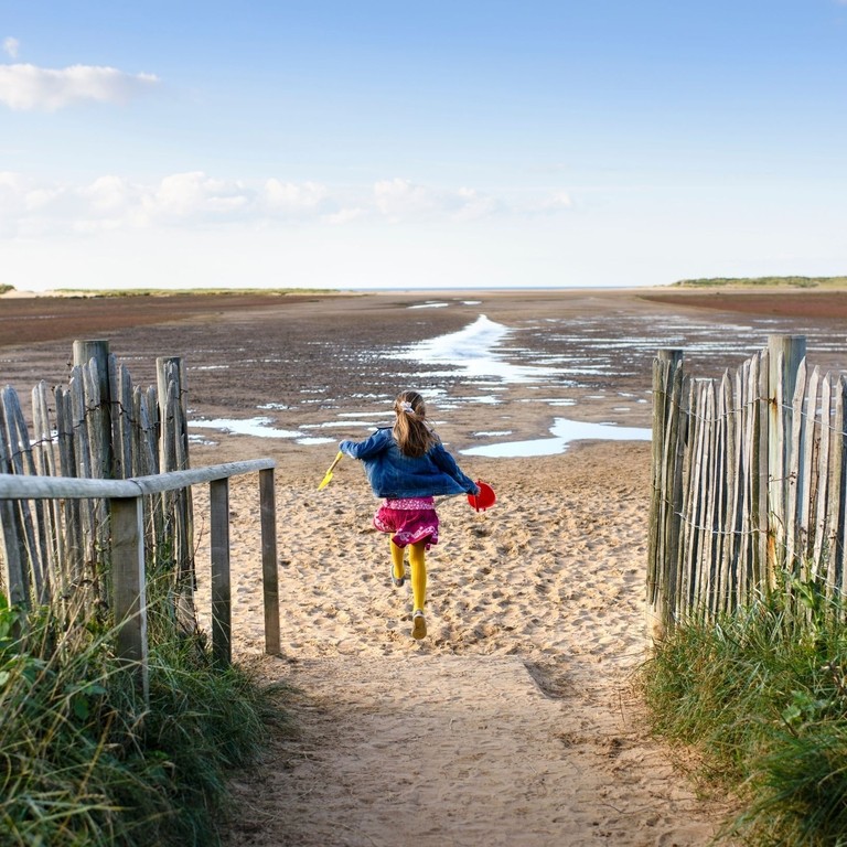 A girl running down a path to Holkham Beach