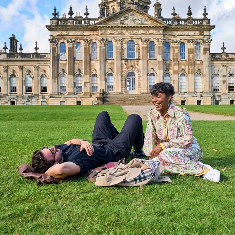 Un homme et une femme se détendent dans l'herbe devant un bâtiment historique.