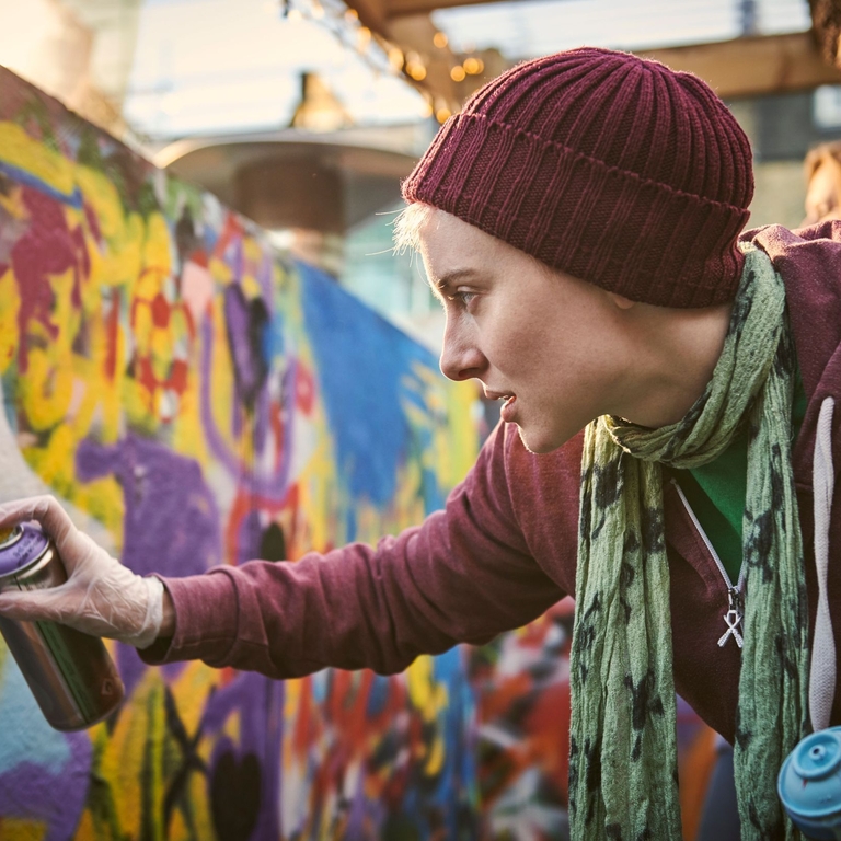 Une jeune femme utilise un aérosol pour créer une peinture murale dans la rue.