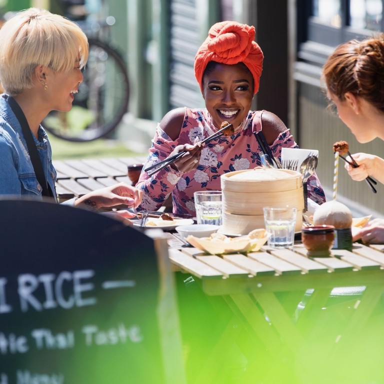 Three young women friends enjoying dim sum lunch at a sunny pavement cafe