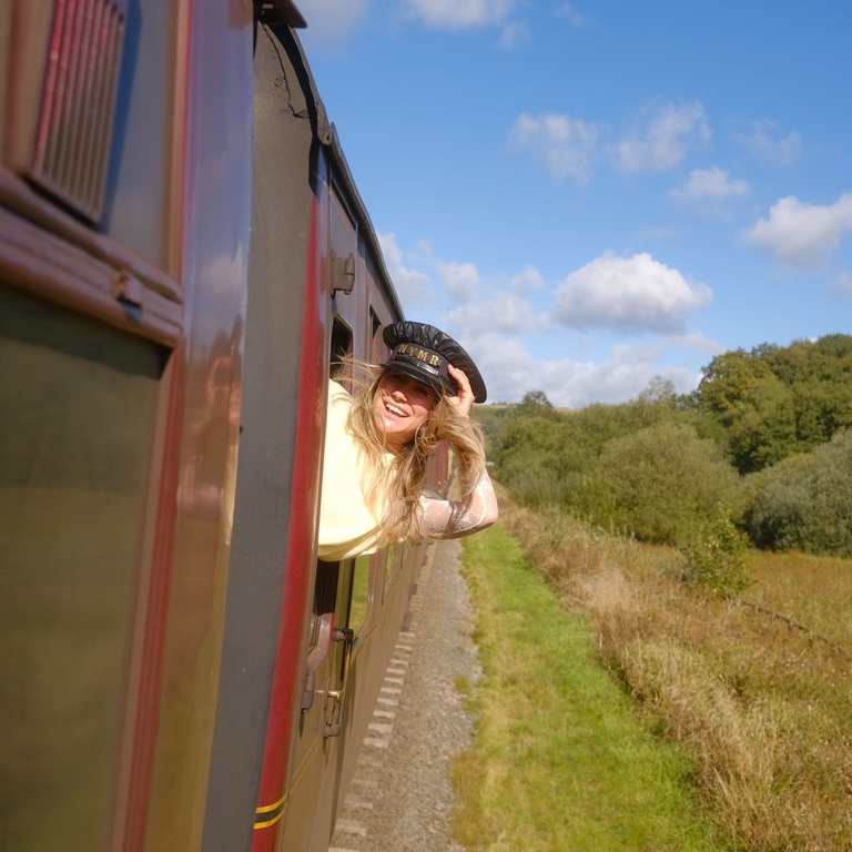 Une femme penchée à la fenêtre d’un train en mouvement traversant la campagne