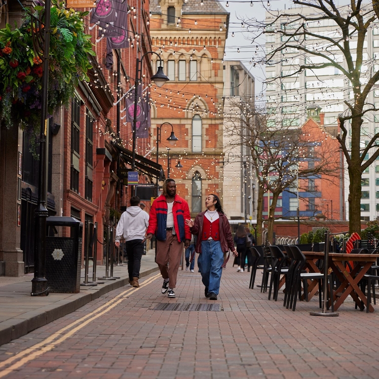 Two men chatting and walking down a street with cafes and a canal.