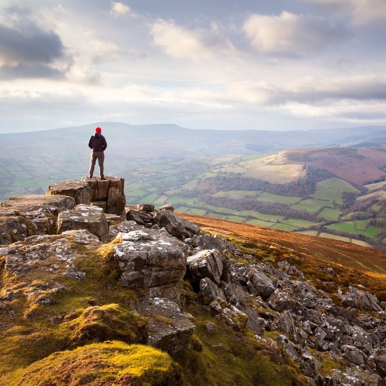 Man atop a vast colourful mountain range at sunset looking out into the valley