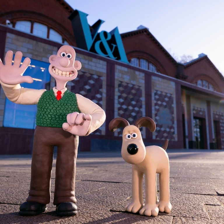 A clay character of a man waving outside a museum alongside a clay dog