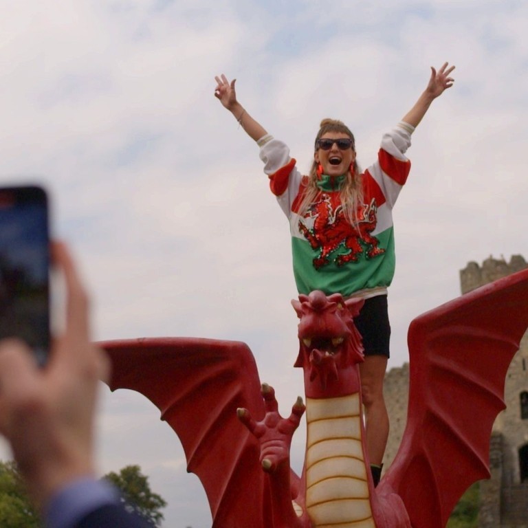 Woman has picture taken standing on a model Welsh dragon.