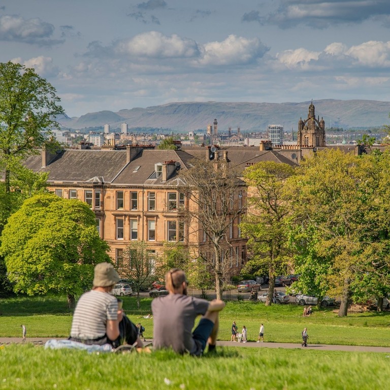 A couple sitting on a hill in a park, over looking a city