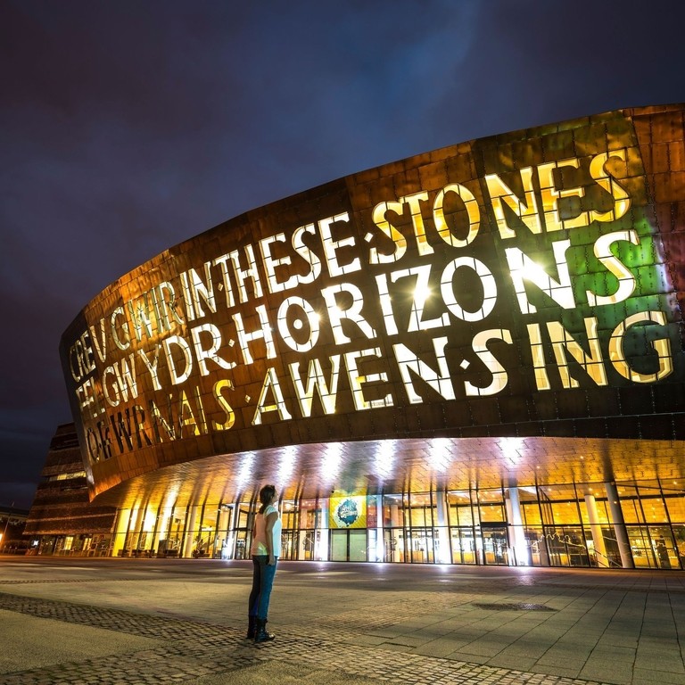 Person looking up at the front of a bronze building at night