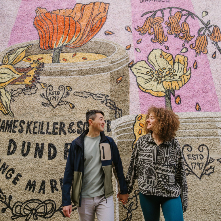 A man and a woman holding hands in front of the marmalade mural.