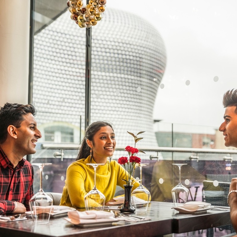 Three young people sat at a dining table with high views