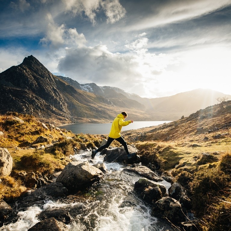 A man jumping across a stream whilst hiking