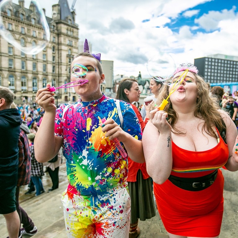Two people celebrating Liverpool Pride by blowing bubbles towards the camera