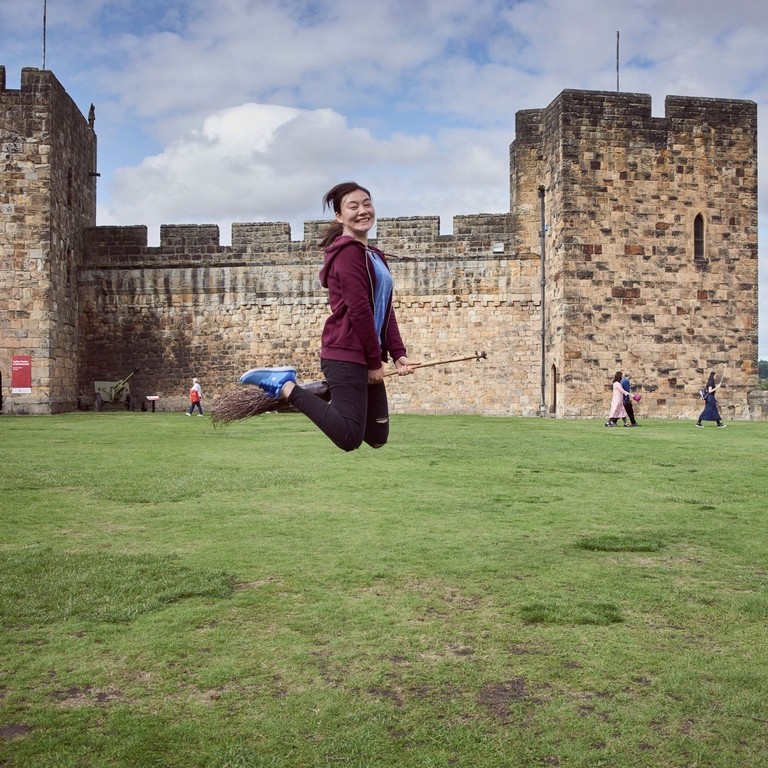 Young woman hovering on a broomstick in the Outer Bailey of Alnwick Castle