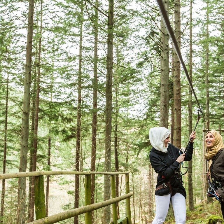 Girls standing on the zipwire platform in the pine forest